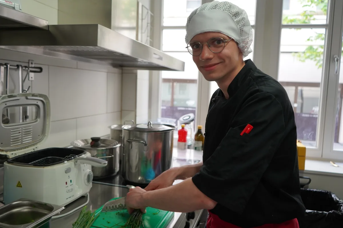 Lukas Adam lächelt mit Kochmütze in die Kamera.